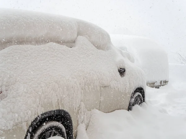 En bil tätt täckt med snö står i en snödriva under kraftigt snöfall. Närbild foto — Stockfoto