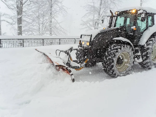 Snow plow tractor clears snowy road during heavy blizzard