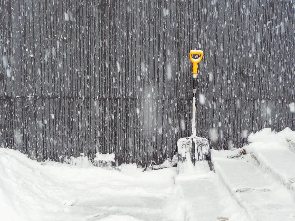 U schodů a plotu stojí lopata se žlutou rukojetí při silném sněžení venku — Stock fotografie