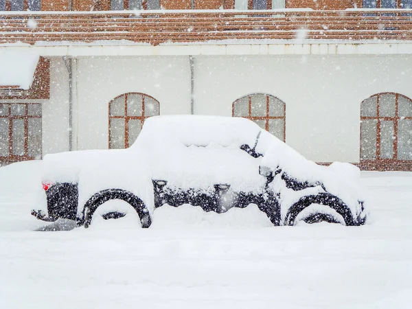 Retro auto stojí pokryté sněhem před budovou během silného sněžení — Stock fotografie