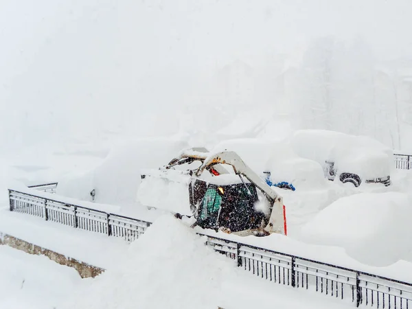 Snöplog traktor och andra fordon tungt täckt med snö på en parkeringsplats under en snöstorm — Stockfoto