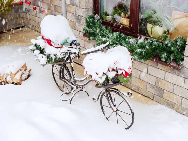 En metall dekorativ cykel täckt med snö står framför ett fönster på gatan under ett snöfall — Stockfoto