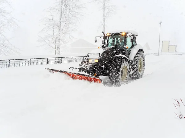 A snow plow tractor clears a snowy road along a fence during a severe blizzard Royalty Free Stock Photos