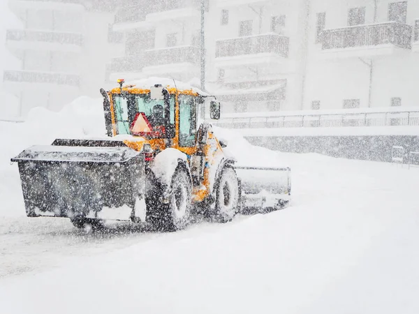 Tractor clears snow from the road in front of the building during heavy snowfall and overcast Stock Photo