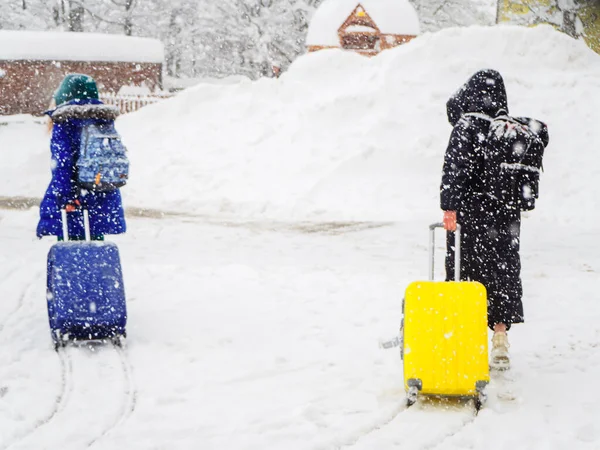 Flickor med ryggsäckar och resväskor går längs den snöiga vägen under kraftiga snöfall. Bilden är ur fokus. Dimmig bildeffekt — Stockfoto