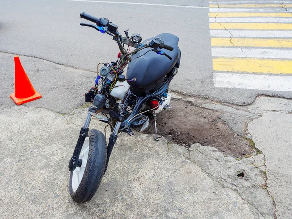 Polorozebraný moped s vystrčenými dráty je zaparkovaný na kraji silnice se zlomeným asfaltem — Stock fotografie