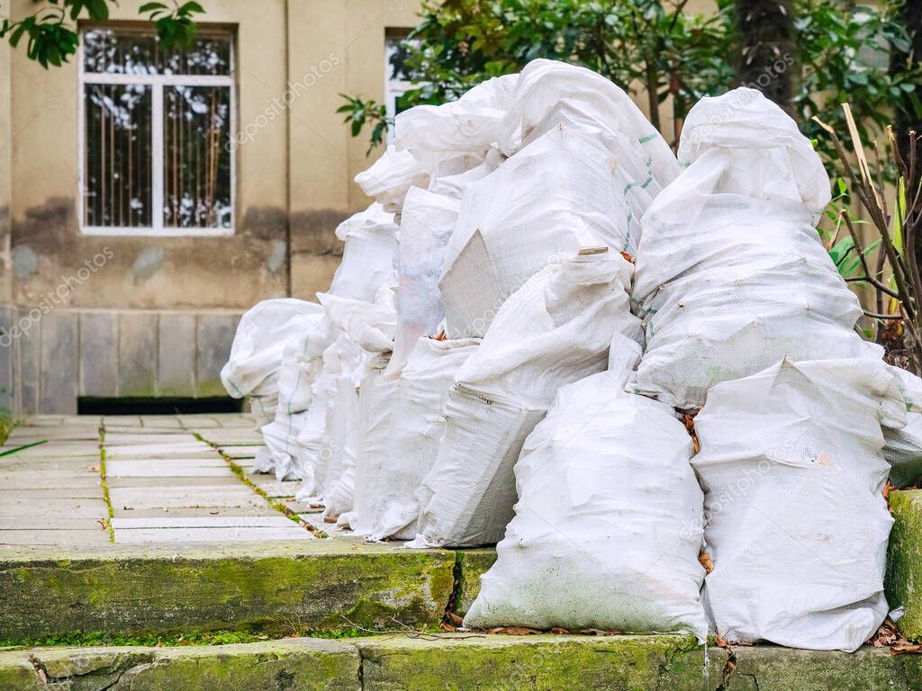 Many identical white bags with unnecessary old rubbish are piled up near the house