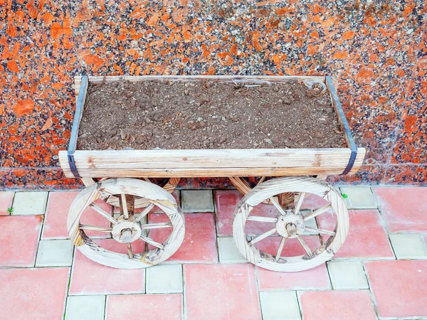 A decorative plant pot in the form of a wooden cart with soil stands near a marble wall — Stock Photo, Image