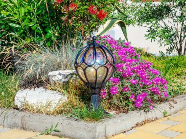 Çiçekleri ve çalıları olan bir çiçek tarhının köşesindeki düşük yuvarlak dekoratif fener.