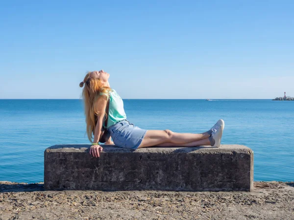 Una chica rubia se sienta en el fondo del mar en una losa de hormigón estirando las piernas — Foto de Stock