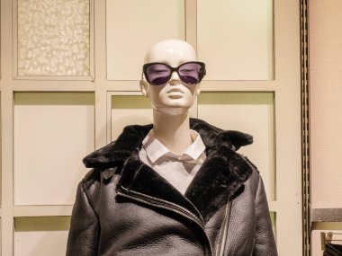 Güneş gözlüğü takan kel bir kadın manken ve kürk yakalı deri ceket.