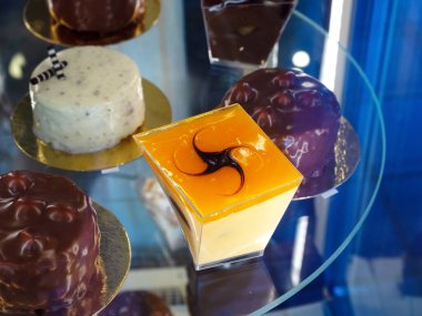 Bir kafede yuvarlak cam bir vitrinde çeşitli tatlı tatlılar duruyor.