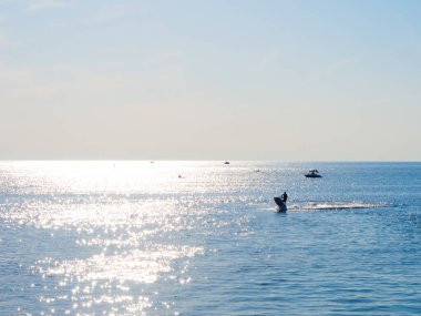 Sakin deniz, güneşli yol, scooter ve uzakta tekneler.