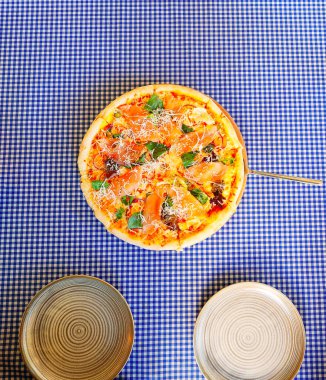 Kırmızı balık peynirli yuvarlak pizza ve iki tabaklı kareli masa örtüsü. Üst görünüm