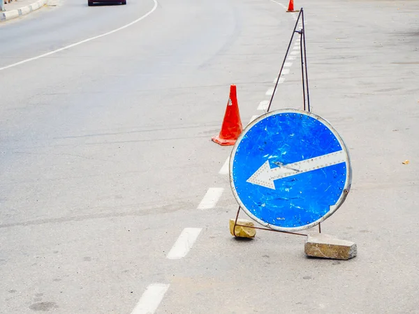Синій круглий знак зі стрілкою і транспортним конусом стоїть на асфальтовій дорозі — стокове фото