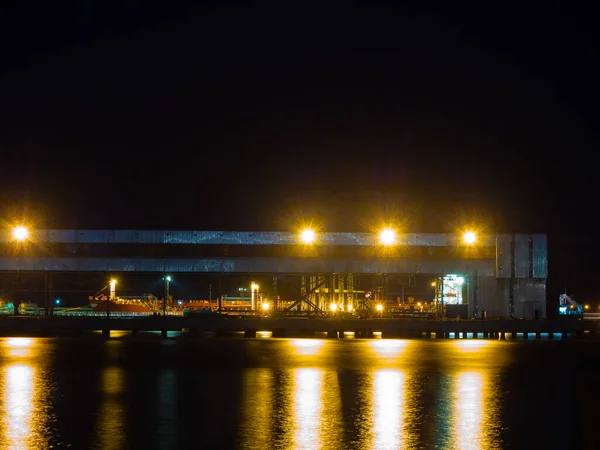 Vista noturna de um porto com uma estrutura metálica iluminada por luzes brilhantes — Fotografia de Stock