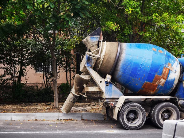 Modrý betonový mixér stojí na kraji silnice u obrubníku na pozadí domu a stromů — Stock fotografie