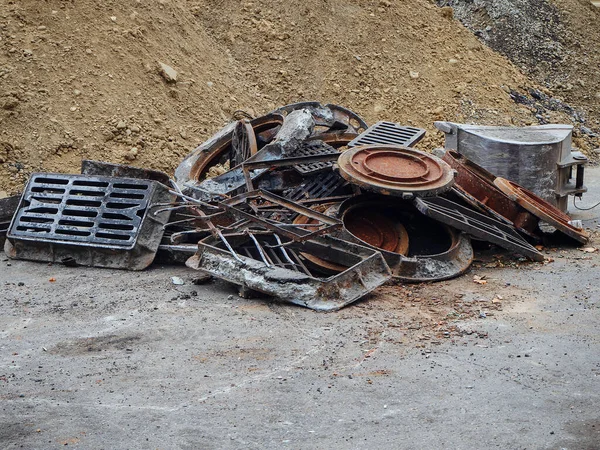 Old rusty metal manhole covers and storm grates piled up near a pile of sand — Stock Photo, Image