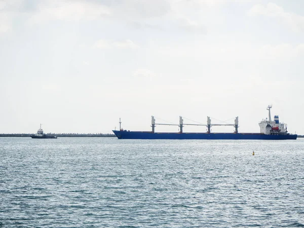 Uma longa balsa azul flutua no mar seguindo um pequeno navio contra um céu nublado — Fotografia de Stock