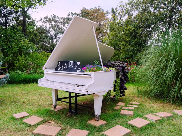 Piano blanco decorativo decorado con flores se encuentra en el parque entre plantas verdes abd árboles —  Fotos de Stock