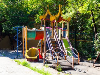 Yeşil ağaçların arka planında kırık ve kirli parçaları olan çocuk parkı.