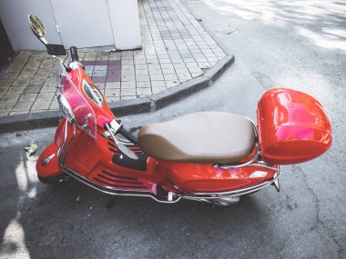 Kırmızı parlak motosiklet yolun köşesinde, kaldırımın kenarında park halinde.