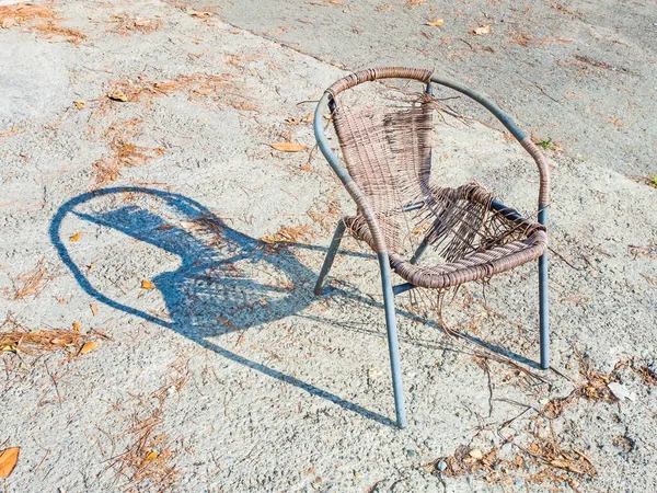 Sebuah kursi tua dengan kerangka logam dan kursi rotan robek berdiri di luar diterangi oleh matahari dan dengan bayangan jatuh dari itu — Stok Foto