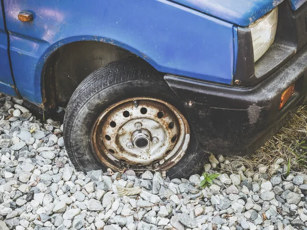 Fragment av en gammal blå bil med ett smutsigt rostigt hjul och en repad stötfångare stående på en sten — Stockfoto