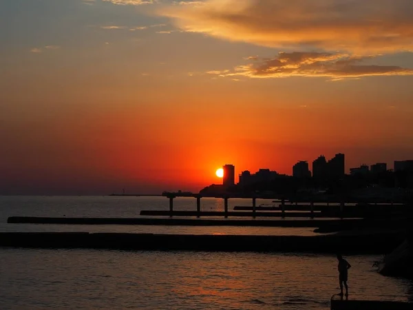 De zon gaat boven de zee en de stad in de heldere zonsondergang hemel onder — Stockfoto