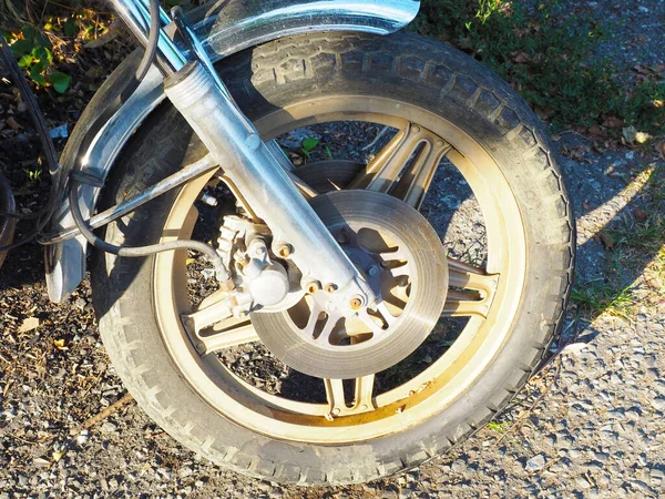 La rueda de una motocicleta de pie sobre asfalto áspero está iluminada por el sol. Foto a pantalla completa. Fragmento de una motocicleta —  Fotos de Stock