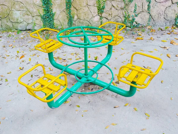 Barnens gröna roterande karusell med gula säten på asfalt strödda med lövverk — Stockfoto