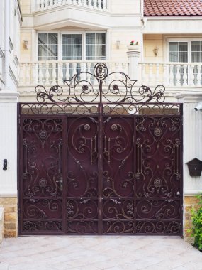 İşlenmiş yaldızlı desenli demir bir bordo çit evin önünde mermer içinde duruyor.