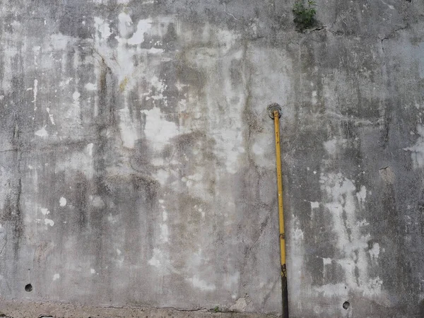A gray concrete wall with dark and light spots and a yellow metal pipe connected to it — Stock Photo, Image
