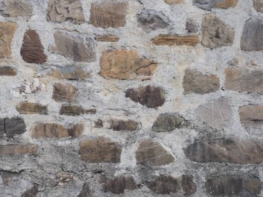 Çeşitli taş şekilli bir duvar ve aralarında kalın gri bir çimento tabakası. Doku kusursuz değil. Yakın plan fotoğraf.