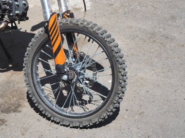 Güneşli bir günde asfaltta duran tozlu bir bisikletin çivili tekerleği.