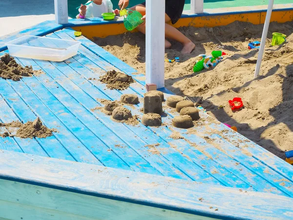 Blue wooden sandbox with sculpted sand cakes and many toys in it