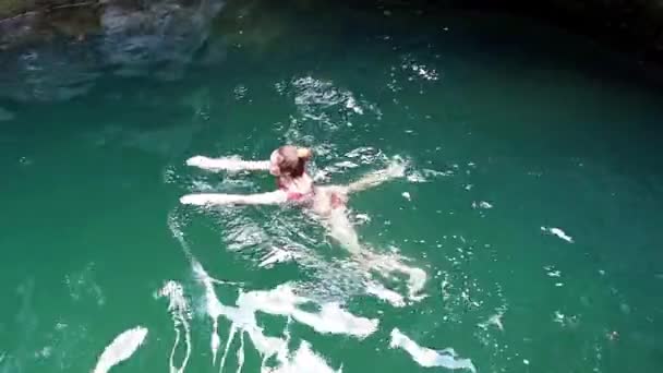 Une fille nage dans une rivière turquoise profonde coulant dans une gorge entre canyons — Video