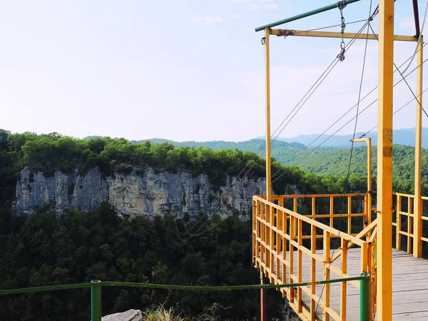 Small observation deck with ropes stretched over the abyss to the rocky and wooded mountains