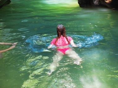 Pembe mayo giyen bir kız, bir vadide açık yeşil bir nehirde yüzüyor.