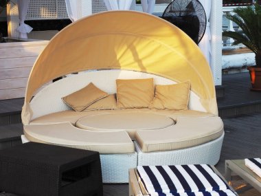 Hafif, yuvarlak, yumuşak yastıklı bir kanepe gölgeli oturma yerinde duruyor.