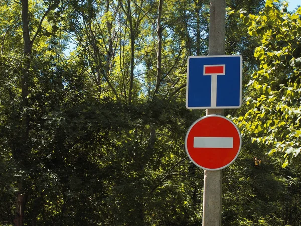 Красно-синие дорожные знаки на шесте на фоне зеленых деревьев. Ограничение движения. Тупик — стоковое фото