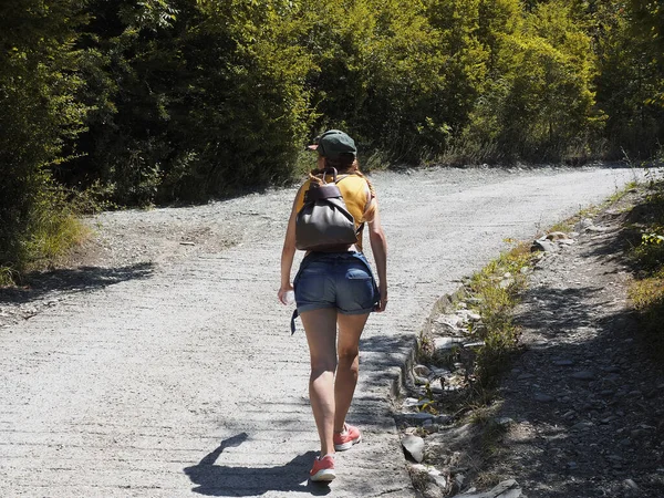 Ένας τουρίστας περπατά κατά μήκος ενός ηλιόλουστου δρόμου κατά μήκος ενός πράσινου δάσους σε μια καλοκαιρινή μέρα. Πεζοπορία — Φωτογραφία Αρχείου