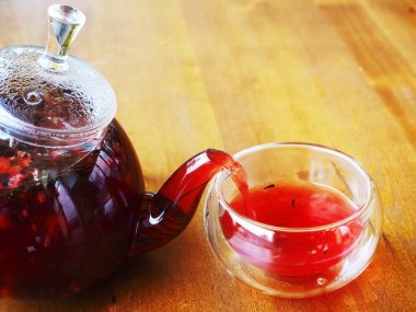 Kırmızı sıcak içecek şeffaf bir çaydanlıktan, tahta bir masada duran bir kaba dökülüyor.