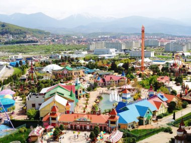 Rusya, Sochi 16.04.2021. Parlak evler ve atlıkarlı arka planda karla kaplı dağlarla Soçi eğlence parkı manzarası. Kuş bakışı