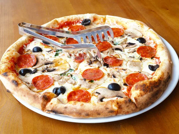 Świeżo upieczona pizza z grzybami, kiełbasą i oliwkami stoi na drewnianym stole. Zdjęcie z bliska — Zdjęcie stockowe