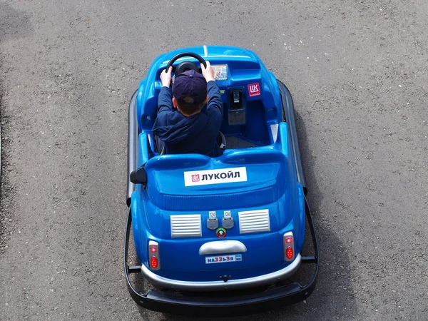 Rusia, Sochi 16.04.2021. El niño monta en un coche azul en miniatura con la inscripción Lukoil. Cartón infantil en el parque de atracciones — Foto de Stock