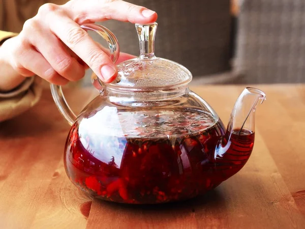 手拿着一个透明的茶壶，上面放着红莓饮料 — 图库照片