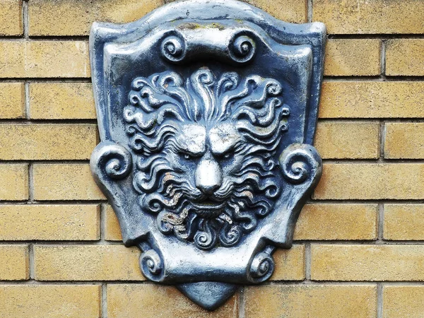 A silver shield with a basrelief lions head on a yellow brick wall