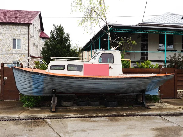 An old boat stands on an iron stand along the fence and private houses on the street on a cloudy day — Stockfoto