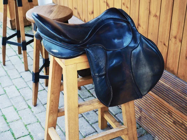 Houten barkruk met een decoratief leren zadel op de stoel in de buurt van de houten bar aan de straat — Stockfoto